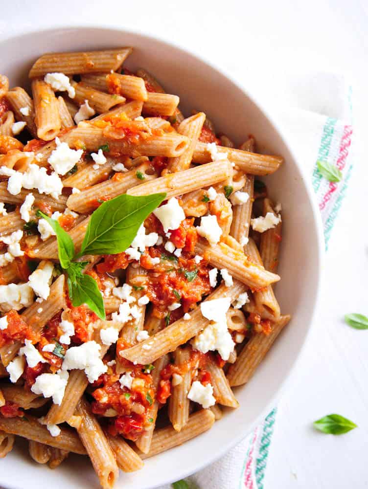 Pasta with sun-dried tomato pesto served in a white bowl.