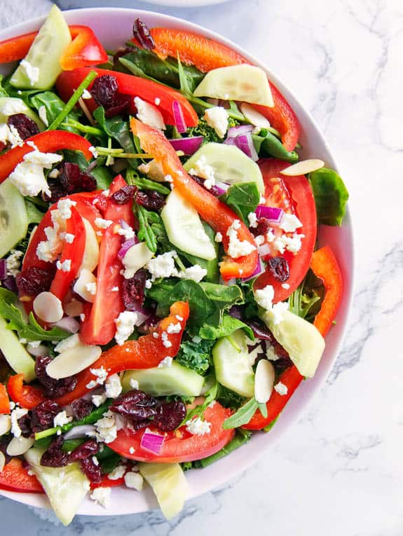 Greek Salad with feta and mixed greens - served in a white bowl against a marble background
