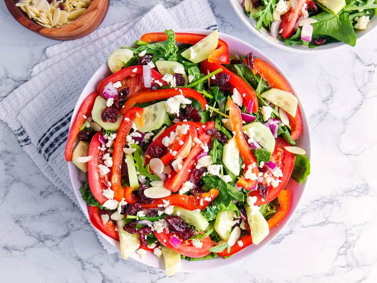 lunchbox makeover: healthy greek salad with peppers, cucumbers, greens, against a white background
