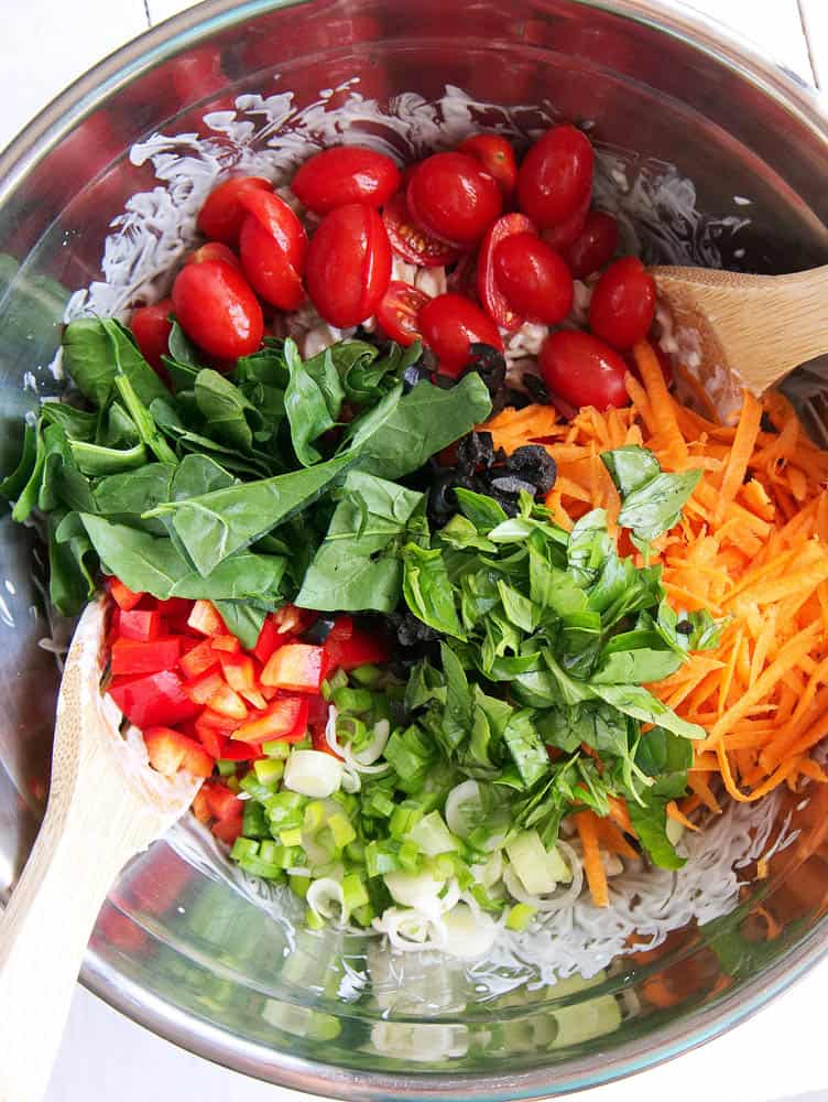 Vegetables being added to the pasta and dressing
