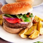 Homemade vegetarian black bean burger on whole wheat bun, topped with baby spinach, tomato, onion and served with home fries on the side