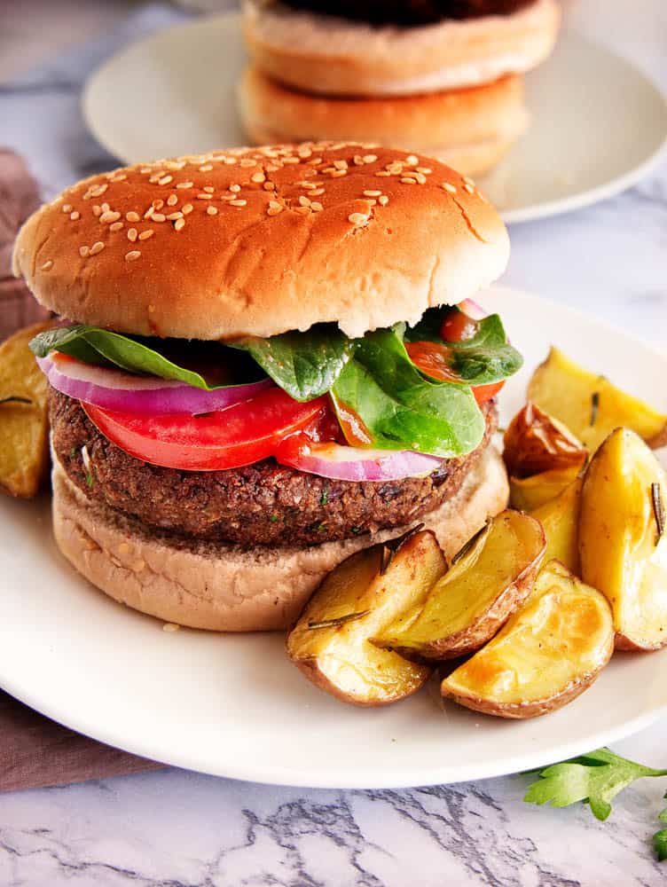 Homemade vegetarian black bean burger on whole wheat bun, topped with baby spinach, tomato, onion and served with home fries on the side