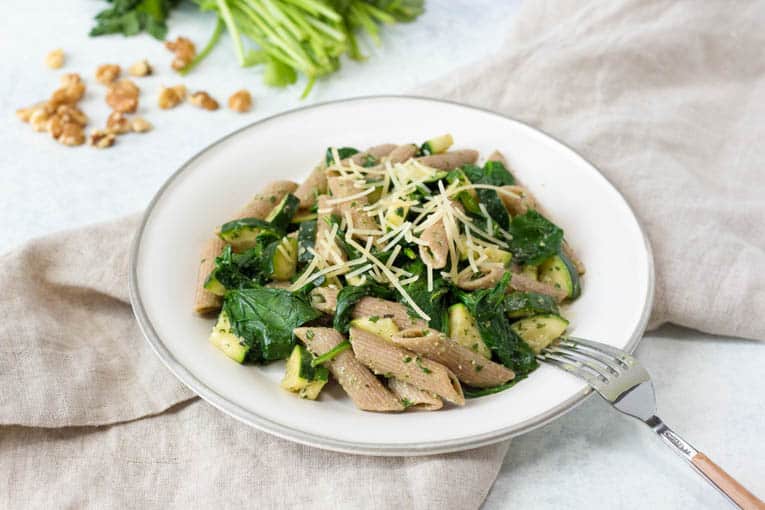 pesto without pine nuts served over whole wheat pasta on a white plate with a fork