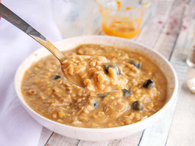 A spoon of Pumpkin Spice Oatmeal with berries and pumpkin being held towards camera