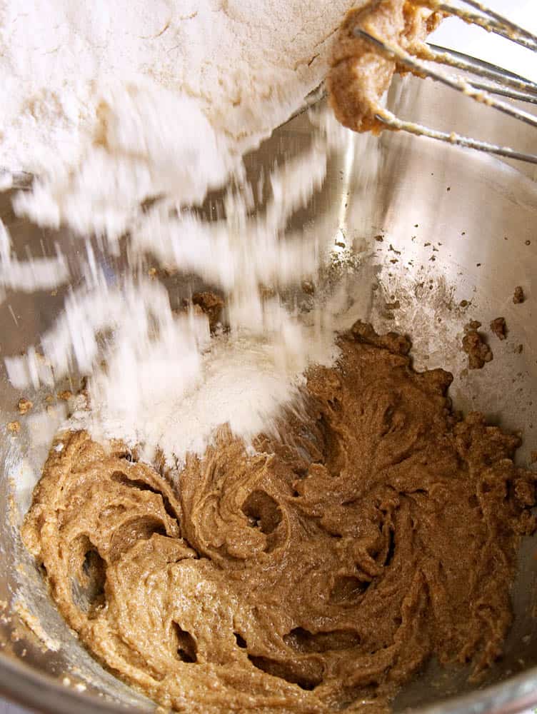Flour being whisked into the sugar mix in a metal mixing bowl. 