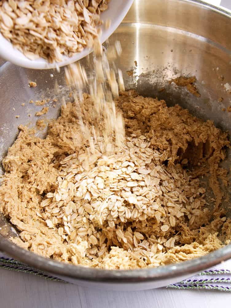 Oats being poured into the bowl of cookie dough. 