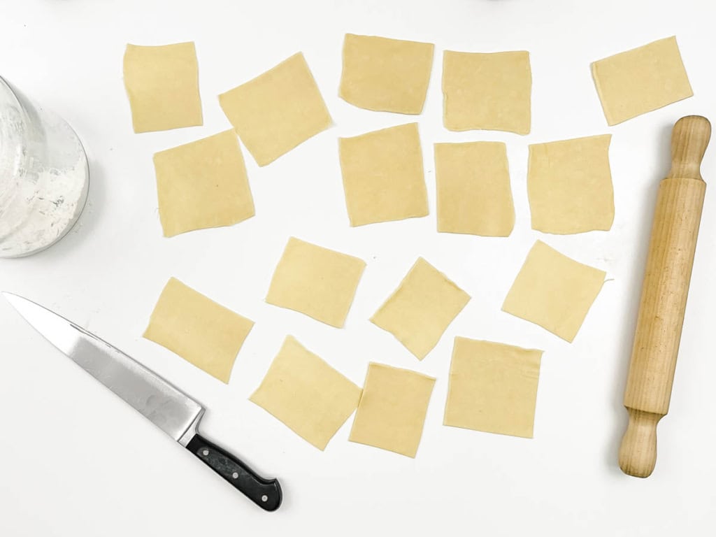 Samosa dough cut into squares on a white countertop.