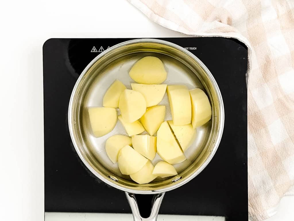 Potatoes boiling in a pot on the stove.