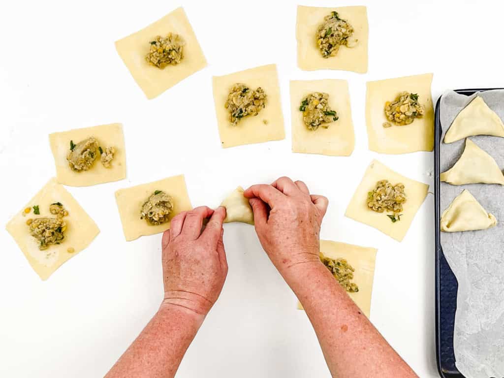 Filling added to samosa dough squares, with hands folding samosas into triangles.