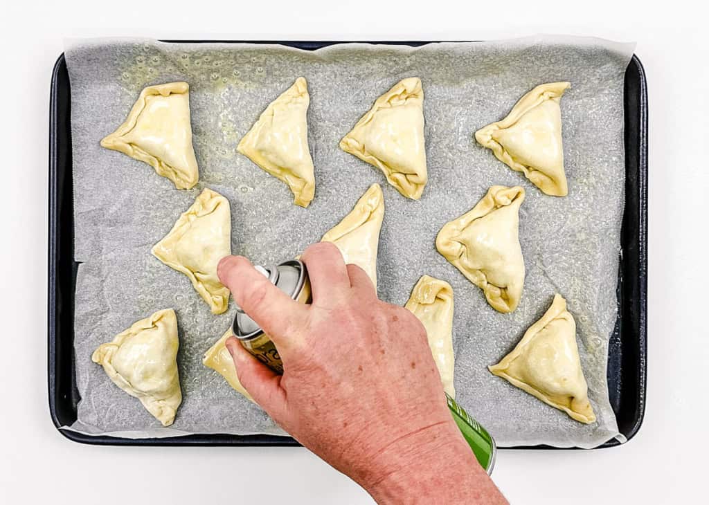 Samosas added to baking sheet and sprayed with cooking spray.