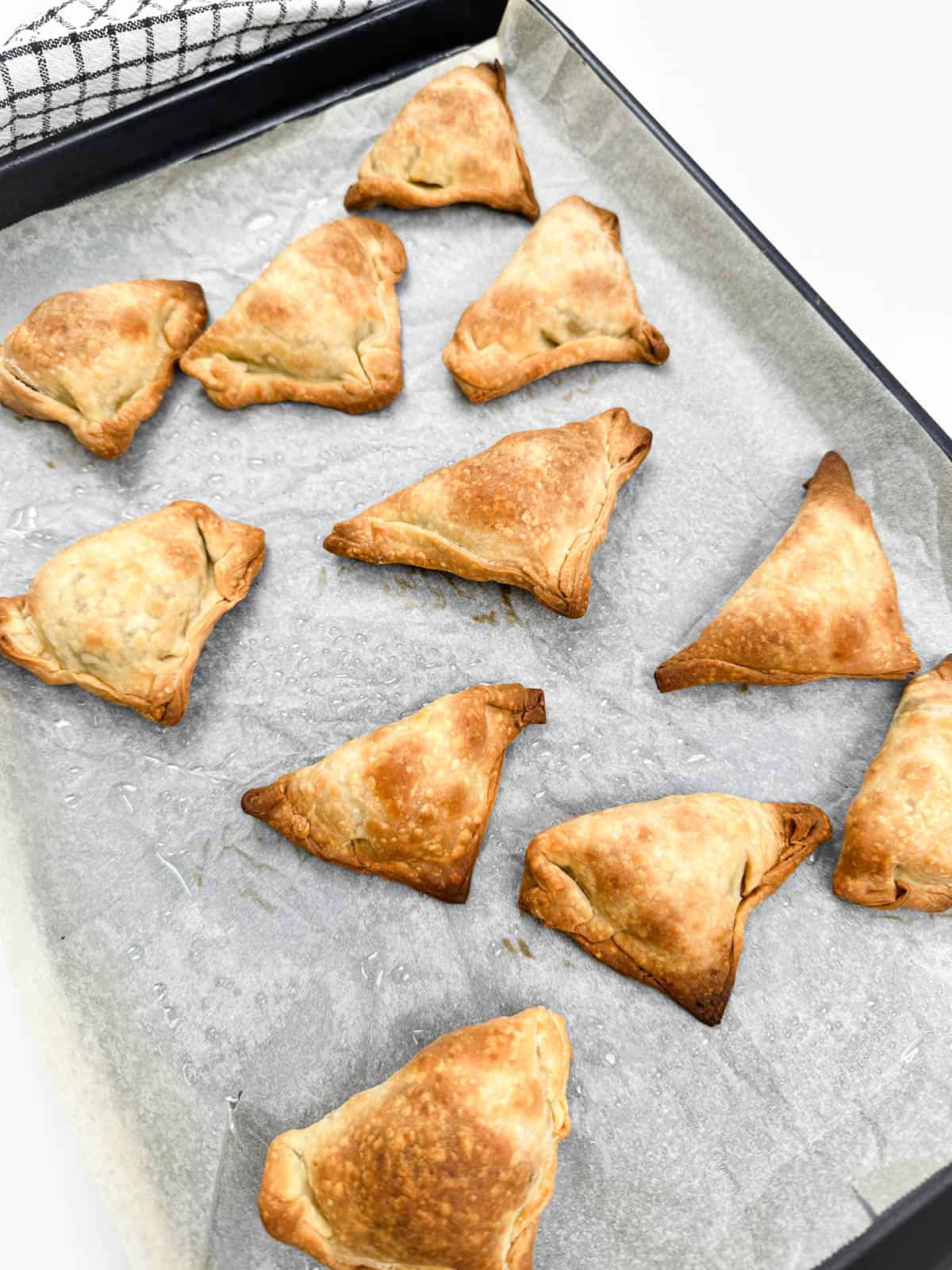 Baked samosas fresh out of the oven on a baking sheet lined with parchment paper.