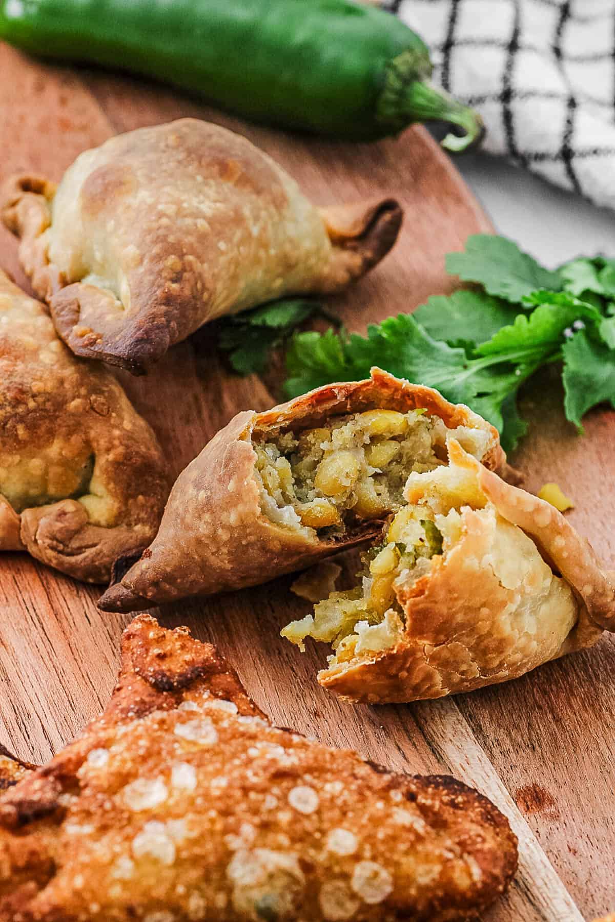 Indian samosas arranged on a cutting board with one samosa cut in half.