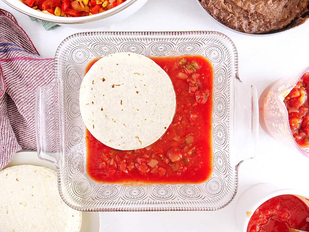 tortillas layered in a baking dish with salsa underneath