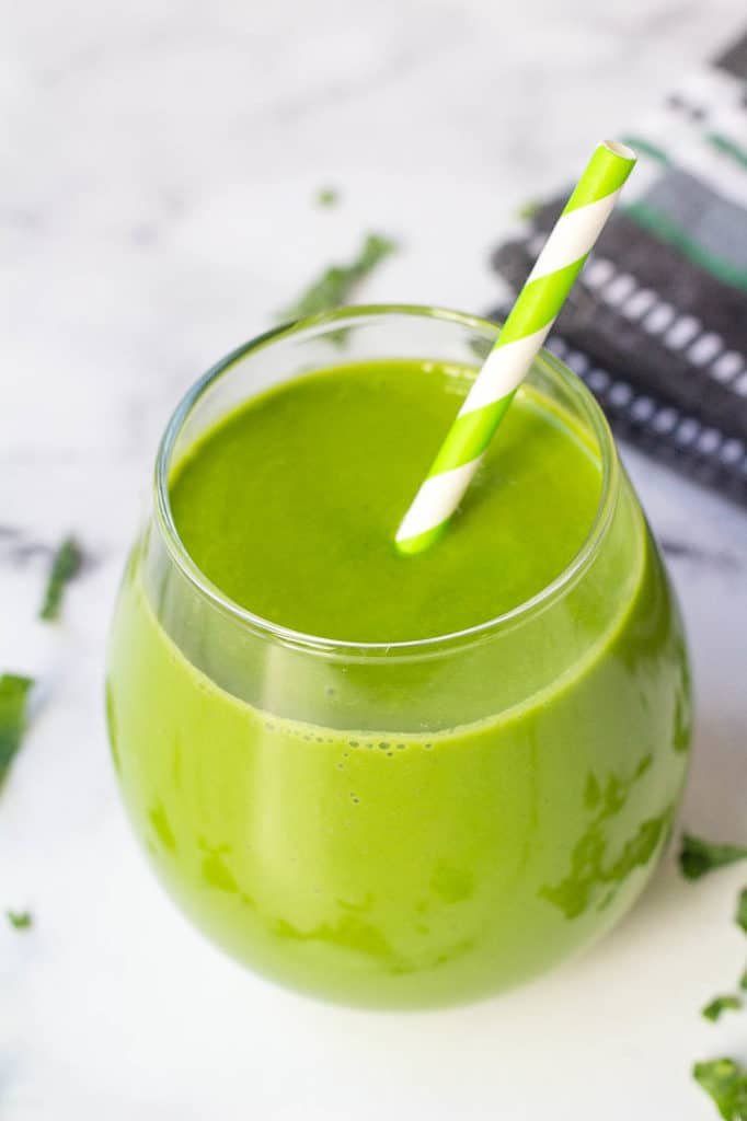 kale smoothie in a glass against a white background with a green and white straw