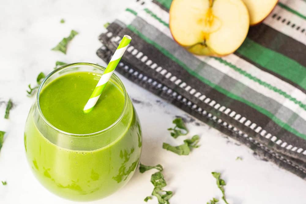 kale smoothie in a glass against a white background with a green and white straw