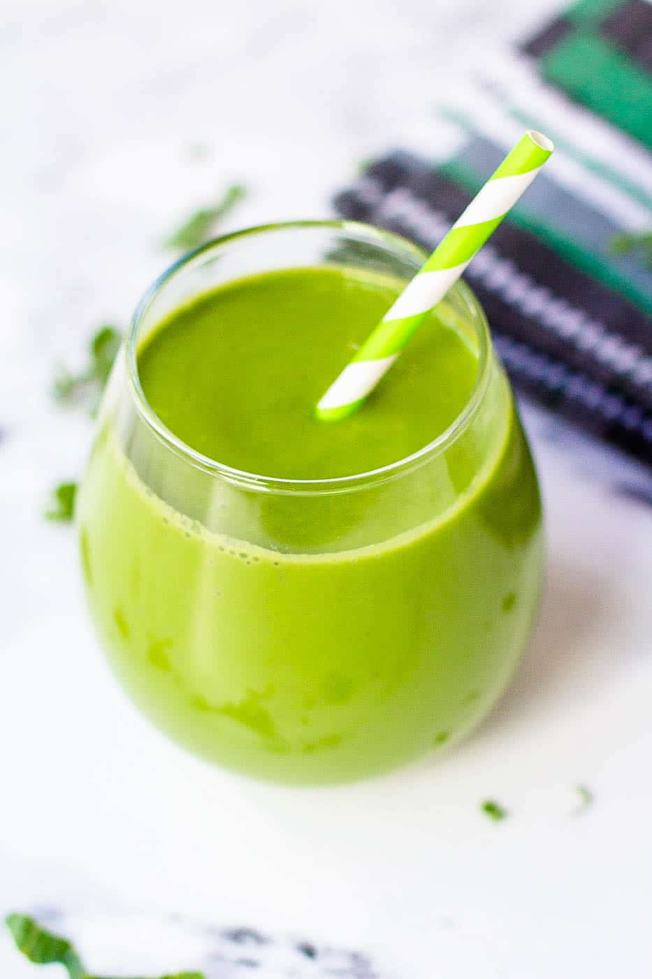 kale smoothie in a glass against a white background with a green and white straw