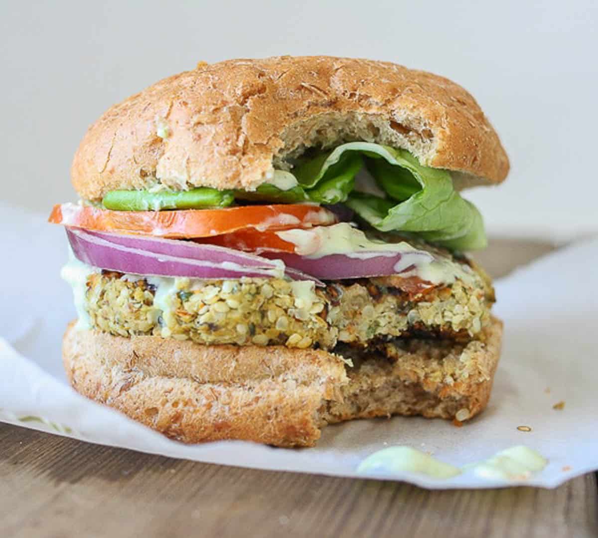 A hemp burger topped with onion, tomato and lettuce in a burger bun, with a bite taken out of it.