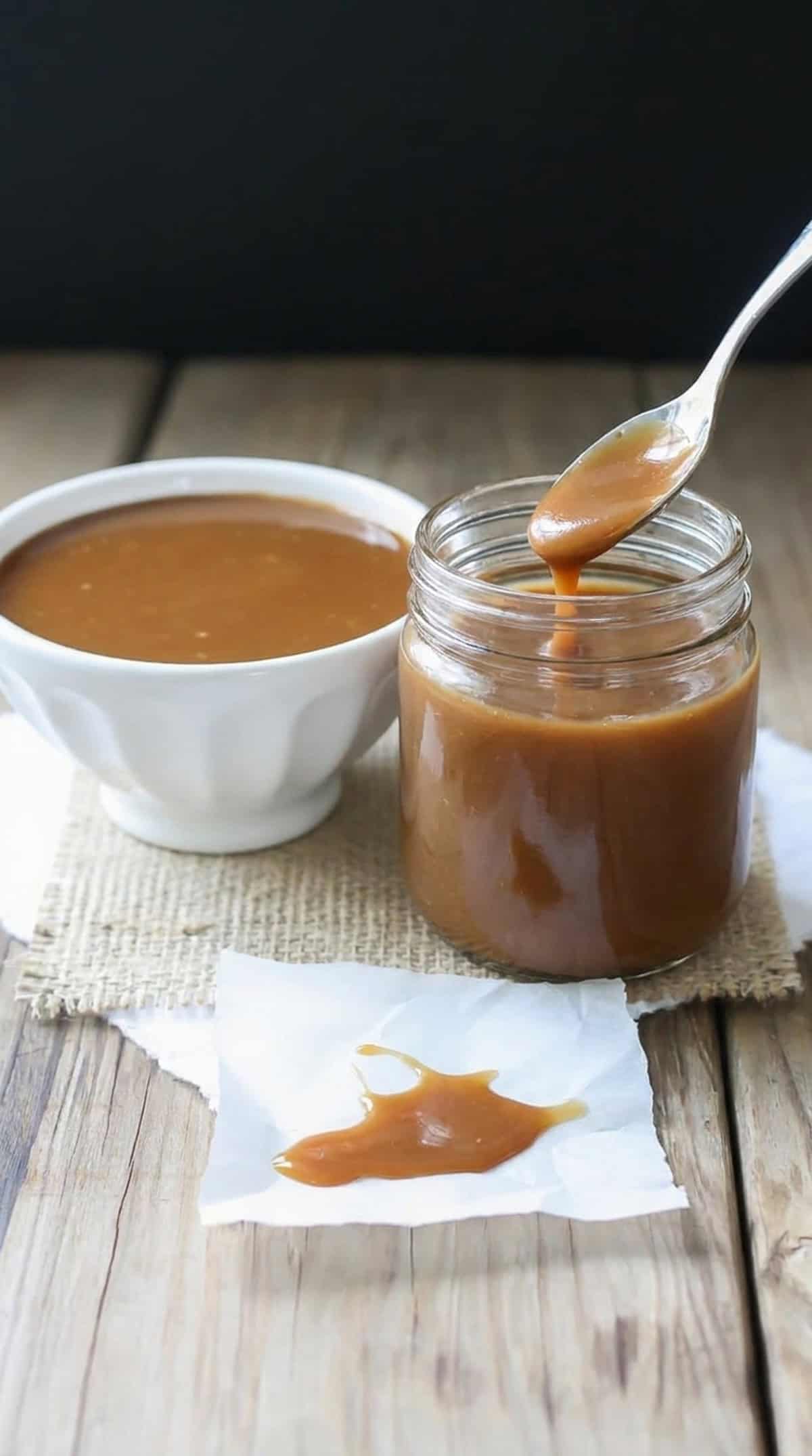 A jar of maple miso dressing with a spoon dipped in it, with a bowl of dressing on the side.