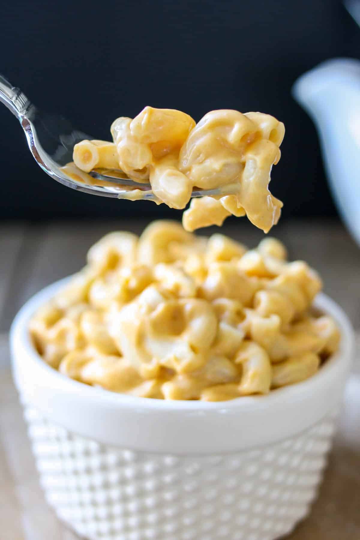 Fork grabbing bite of orange creamy mac and cheese from white bowl