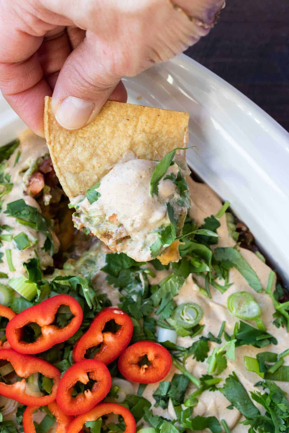 Vegan taco sauce served as part of a 7 layer dip, being scooped up with a tortilla chip.