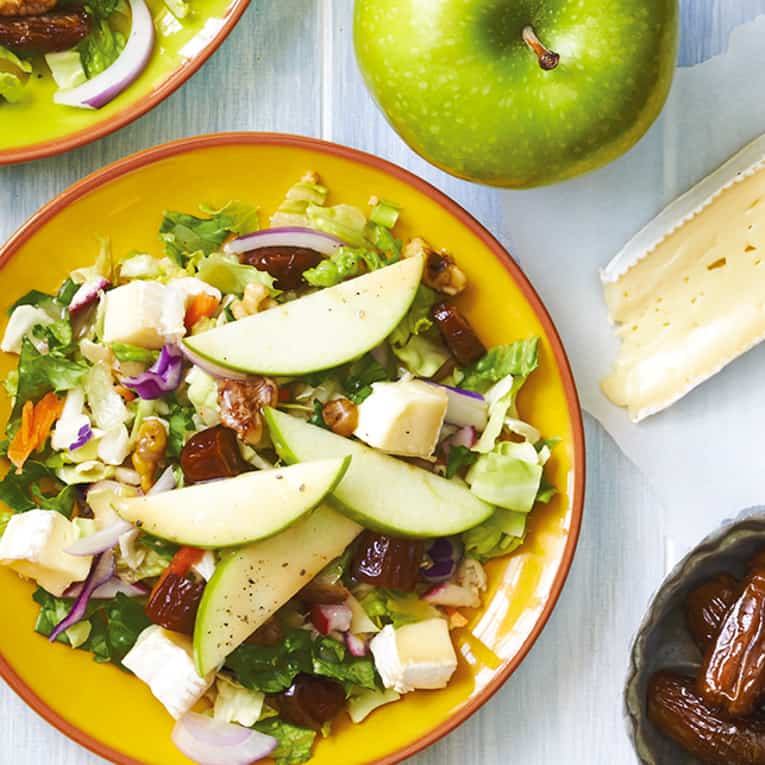 top view of apple walnut salad with dates and brie pictured on a yellow plate