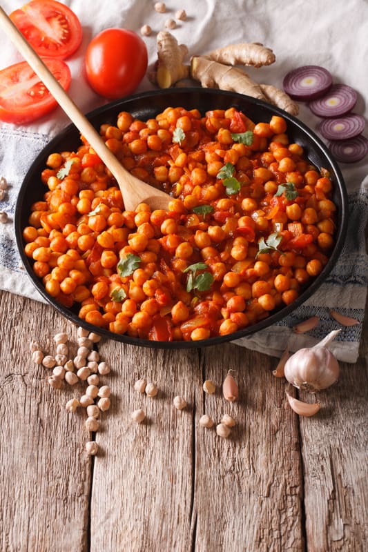 vegan chana masala recipe, served in a black bowl with tomatoes and onions as garnishes on the side. top view. 
