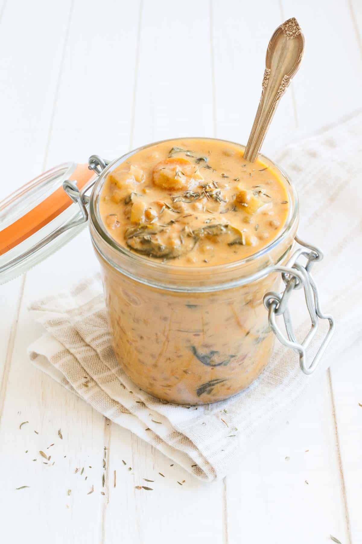 Rich and creamy vegan lentil stew to warm you from the inside out. Full of healthy ingredients and anti-inflammatory benefits, to make a perfect cozy meal! #vegansoup #healthyveganrecipes Top side view of orange colored lentil and veggie stew in a glass jar
