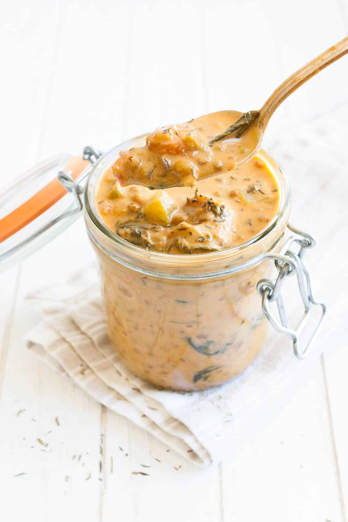 Rich and creamy vegan lentil stew to warm you from the inside out. Full of healthy ingredients and anti-inflammatory benefits, to make a perfect cozy meal! #vegansoup #healthyveganrecipes Spoon taking some orange colored lentil stew from a glass jar
