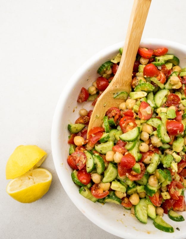 chickpea tomato feta salad Top shot of avocado cucumber tomato salad in a bowl with a serving spoon
