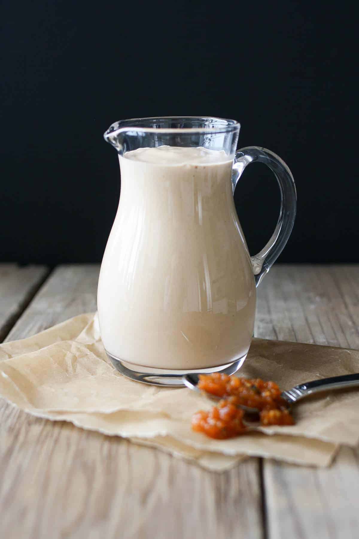 A glass pitcher filled with a light pink sauce on a wooden table