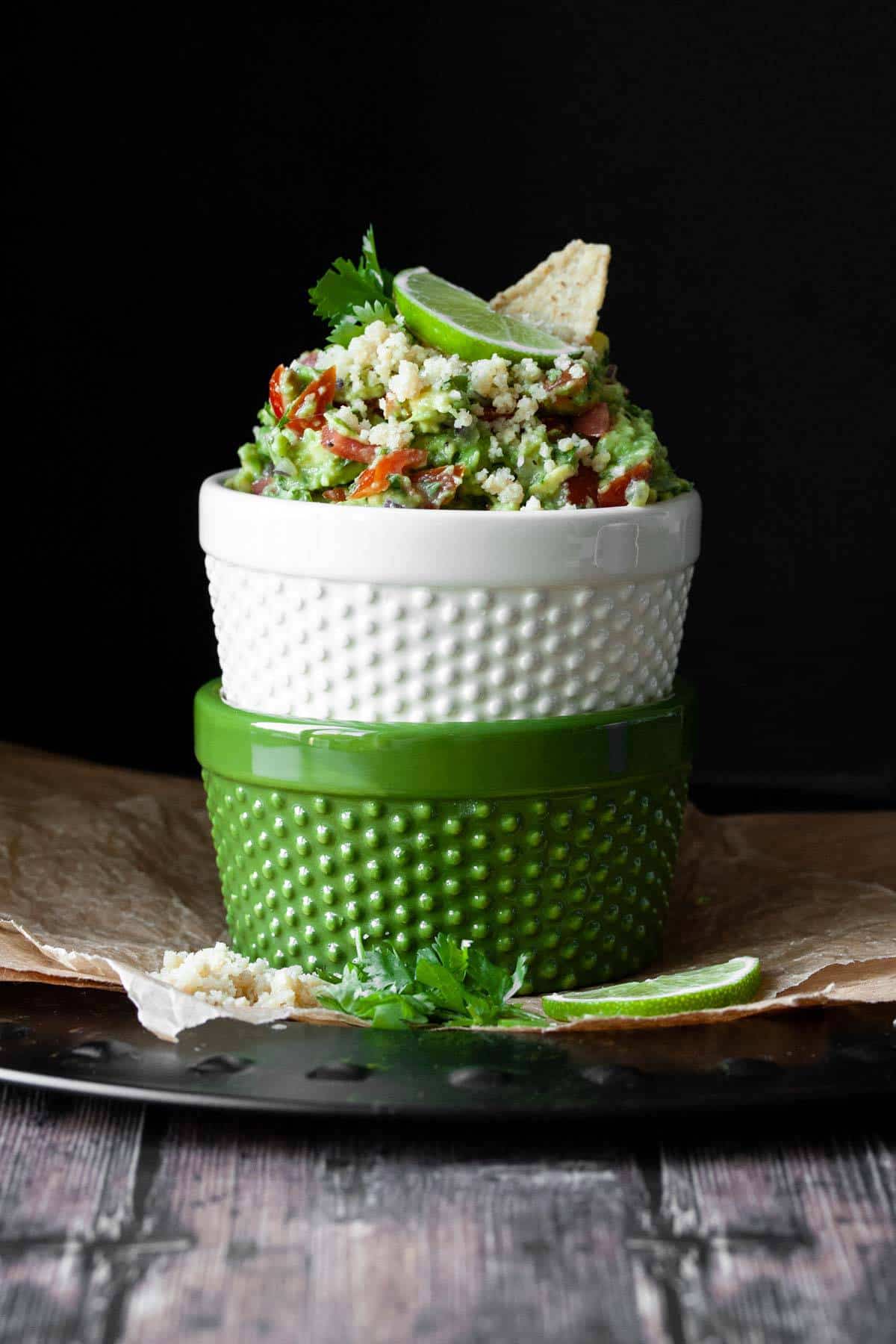 Two bowls stacked on top of each other and top one filled with fully loaded guacamole with vegan cotija cheese
