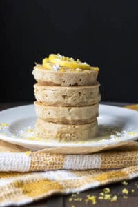 Stack of vegan lemon pancakes topped with lemon slices, powdered sugar and glaze.