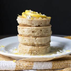 Stack of vegan lemon pancakes topped with lemon slices, powdered sugar and glaze.