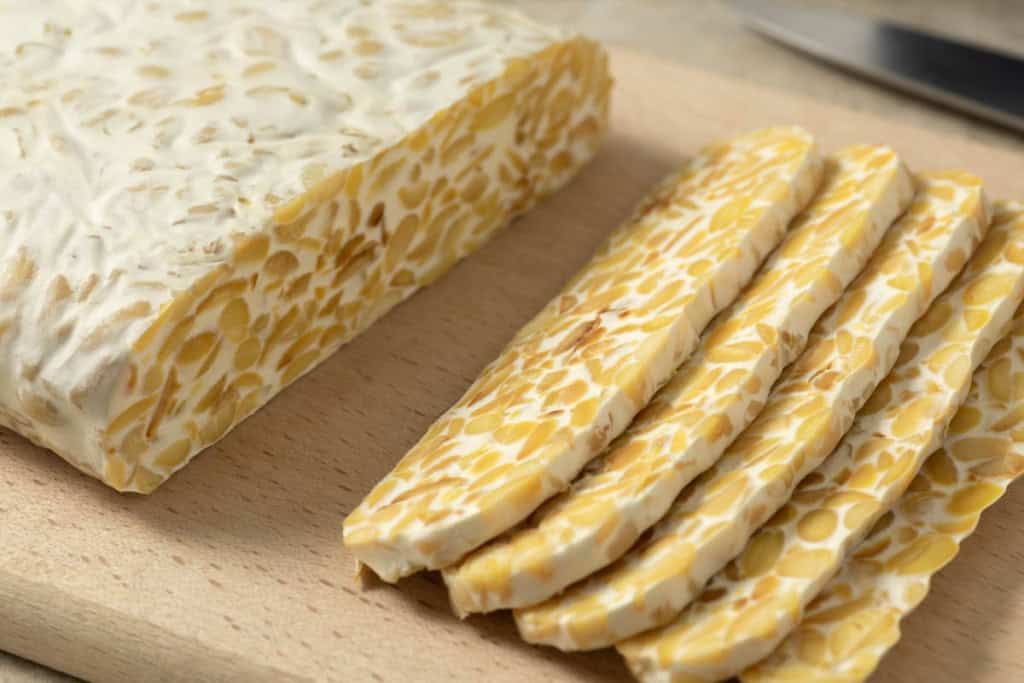 Traditional vegetarian tempeh sliced on a cutting board close up.