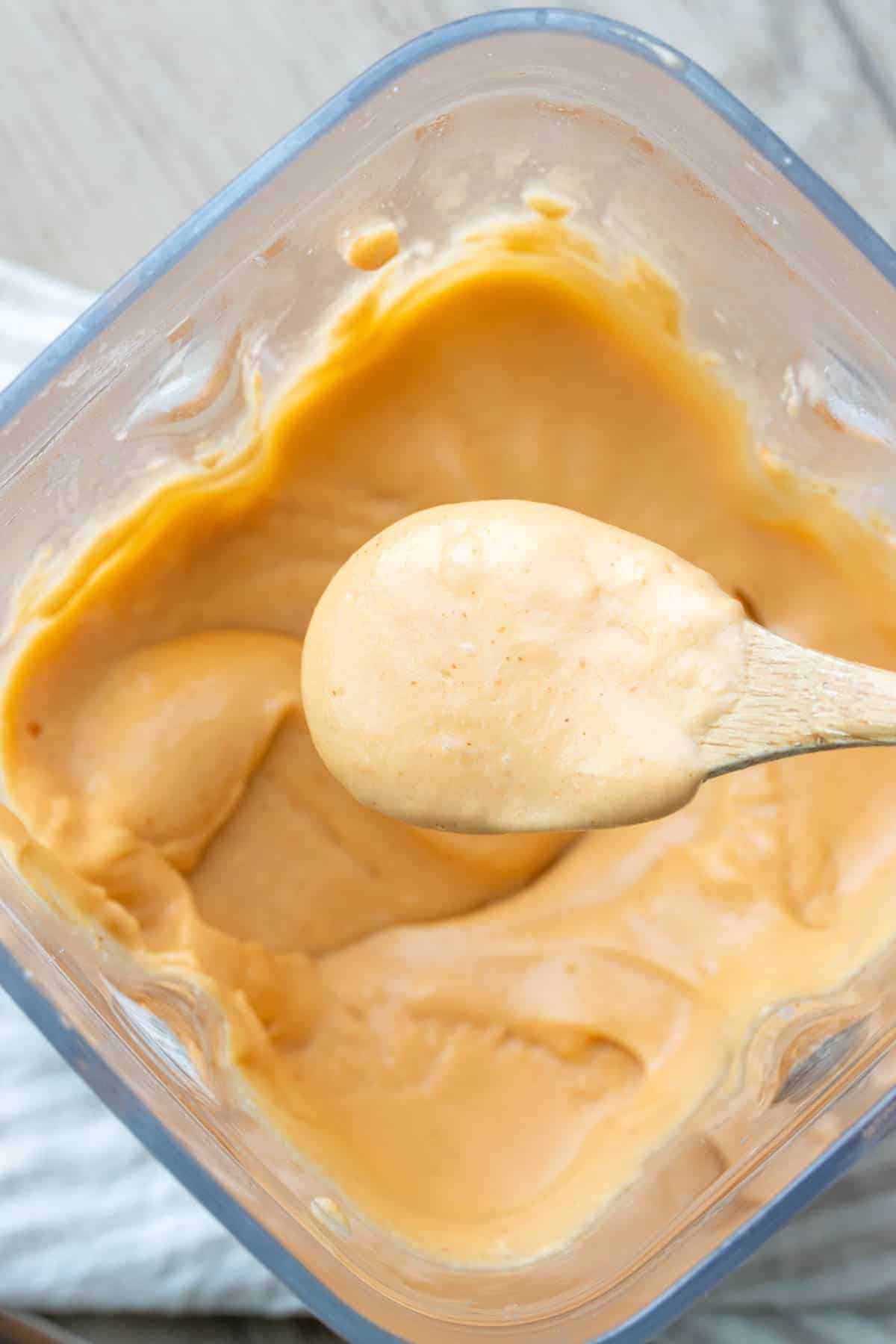 Spoon dipping into a blender filled with orange cheese sauce and grabbing a scoop out