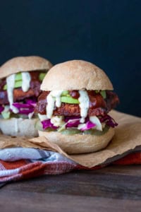 Front view of a BBQ tempeh sandwich in a bread roll with cabbage, avocado, pickles and ranch, on a cutting board.