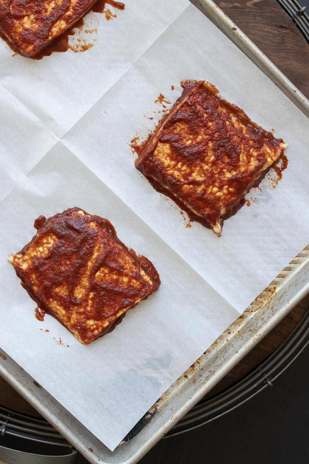 Squares of tempeh slathered in BBQ sauce on a parchment lined cookie sheet.