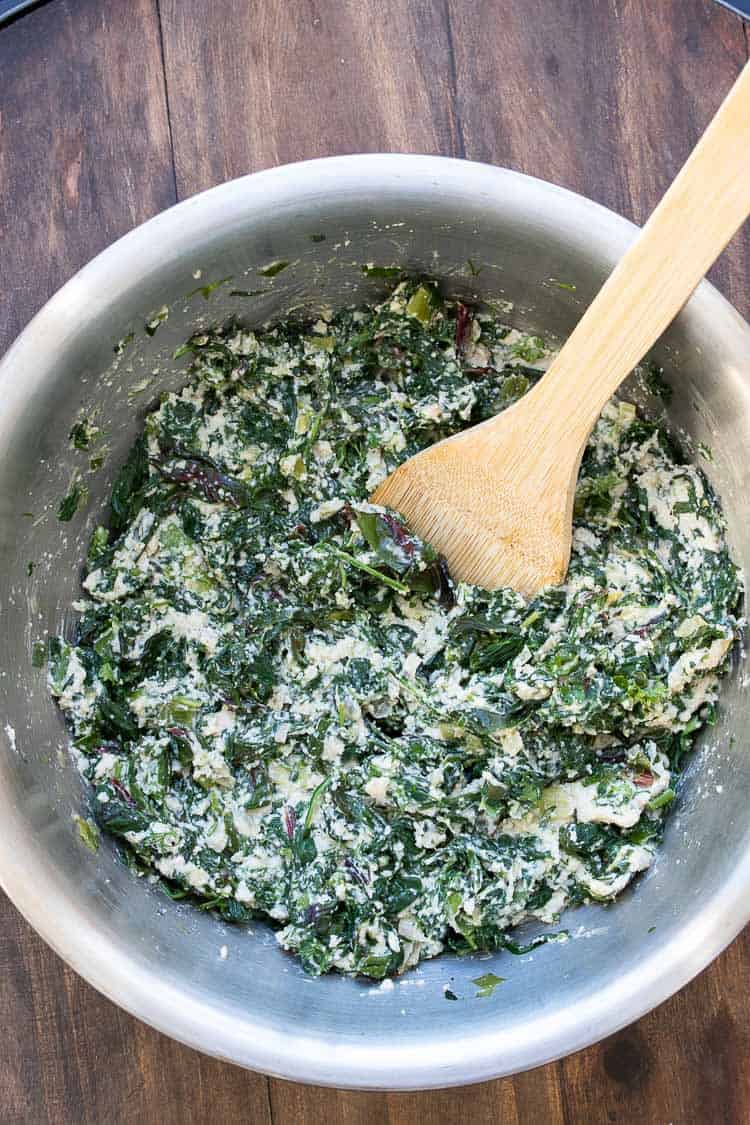 This authentic Greek recipe has gotten a makeover and is better than ever. This vegan spanakopita is hands down the absolute best you've ever had! #veganappetizers #greekrecipes Filling of sautéed spinach and chopped creamy cashew mixture in a silver bowl