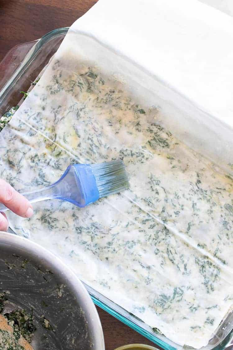 This authentic Greek recipe has gotten a makeover and is better than ever. This vegan spanakopita is hands down the absolute best you've ever had! #veganappetizers #greekrecipes Spanakopita being constructed with layered phyllo (filo) sheets in a glass baking dish