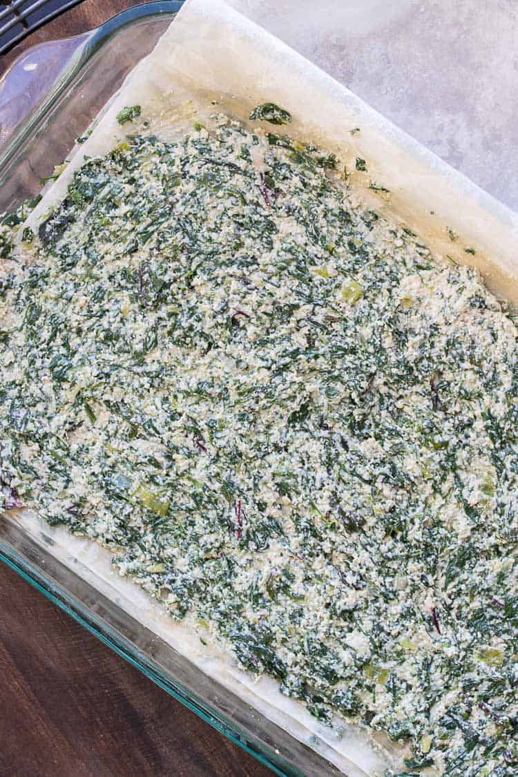 This authentic Greek recipe has gotten a makeover and is better than ever. This vegan spanakopita is hands down the absolute best you've ever had! #veganappetizers #greekrecipes Spinach and chopped creamy cashew mixture spread over phyllo (filo) sheets layered in a glass baking dish
