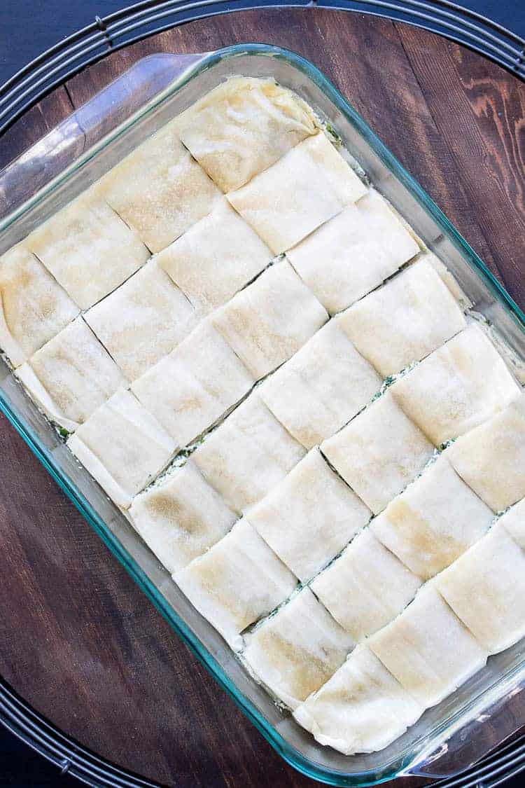 This authentic Greek recipe has gotten a makeover and is better than ever. This vegan spanakopita is hands down the absolute best you've ever had! #veganappetizers #greekrecipes Cut squares of unbaked spanakopita in a glass baking dish