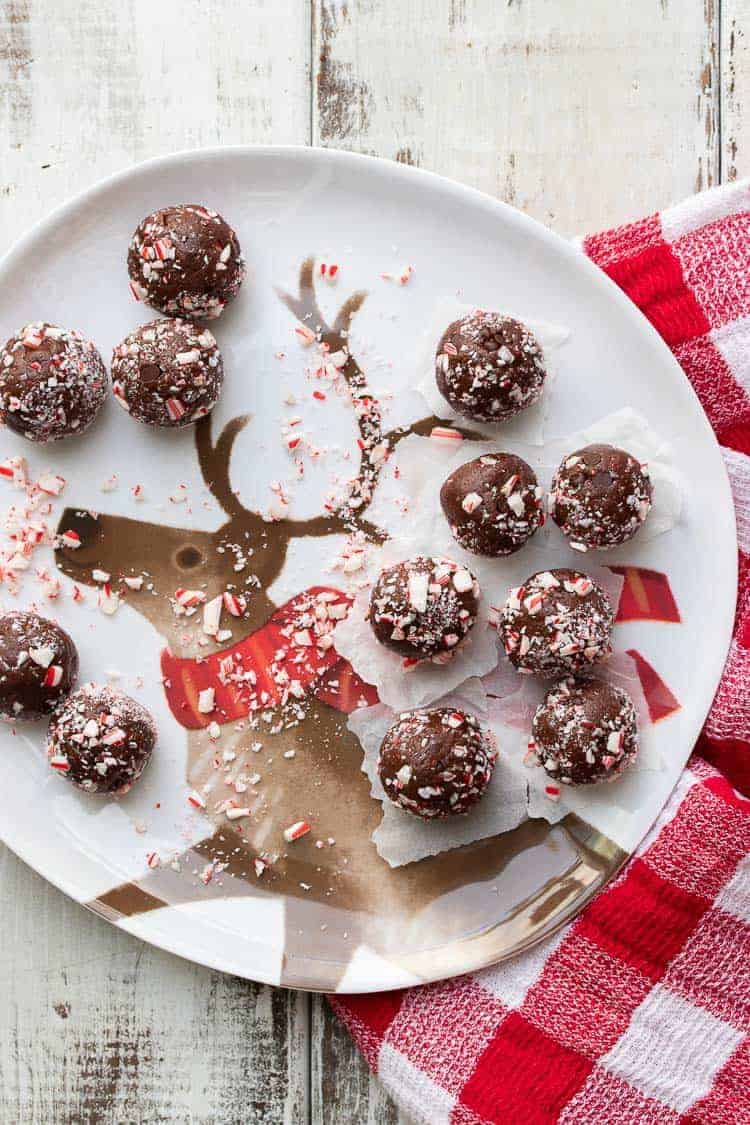 A festive vegan holiday treat made in only 5 minutes! These no bake chocolate peppermint balls even have a trick to keeping them whole food and healthy. #vegandessertrecipes #veganchristmas Candy cane covered brownie balls on a white plate with a reindeer on it