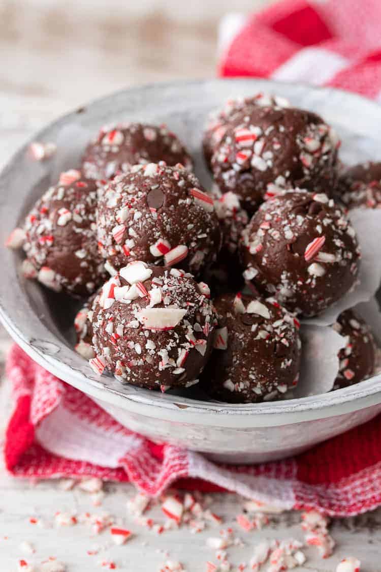 A festive vegan holiday treat made in only 5 minutes! These no bake chocolate peppermint balls even have a trick to keeping them whole food and healthy. #vegandessertrecipes #veganchristmas White bowl filled with chocolate peppermint candy cane balls on a red checkered towel