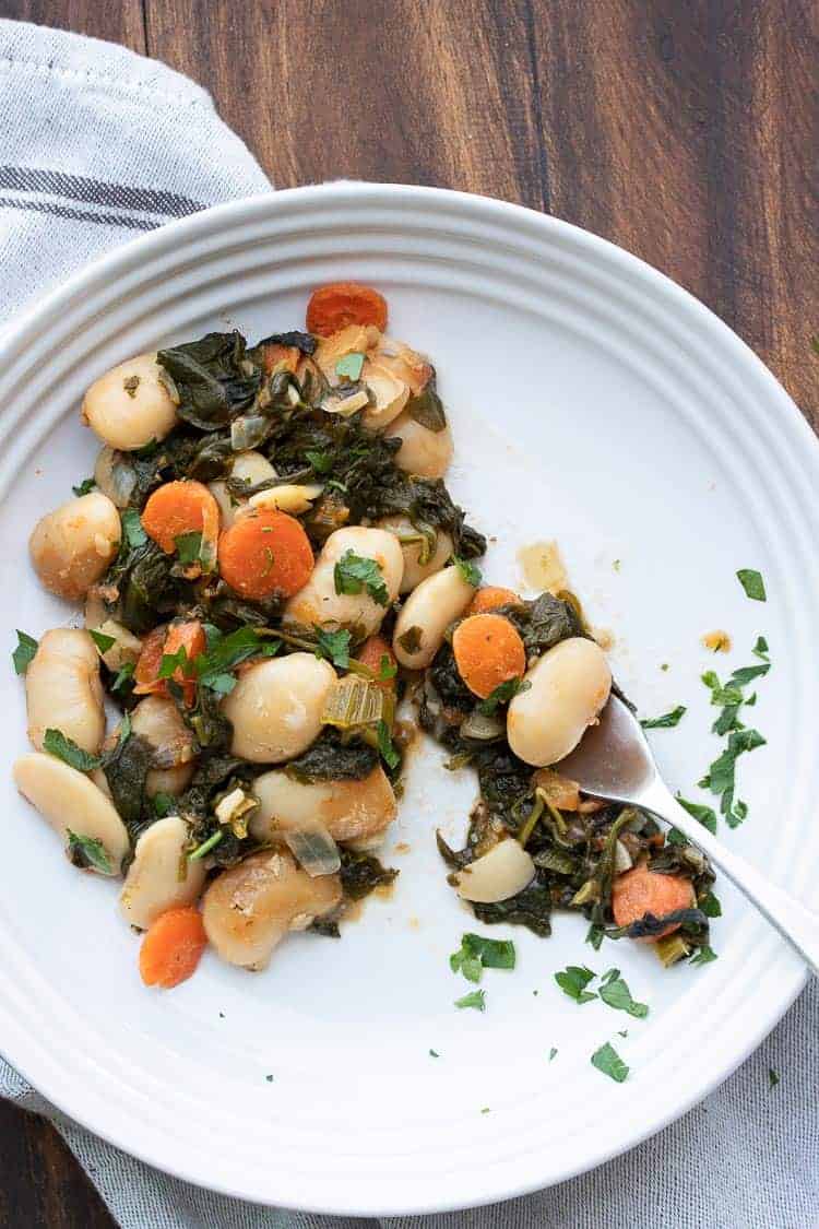 This healthy lima bean recipe with added veggies is a one stop meal. Gigantes Plaki is loaded with protein, perfect for all ages and so flavorful! #limabeanrecipes #greekrecipes Fork eating a bite out of a plate of baked lima beans and veggies