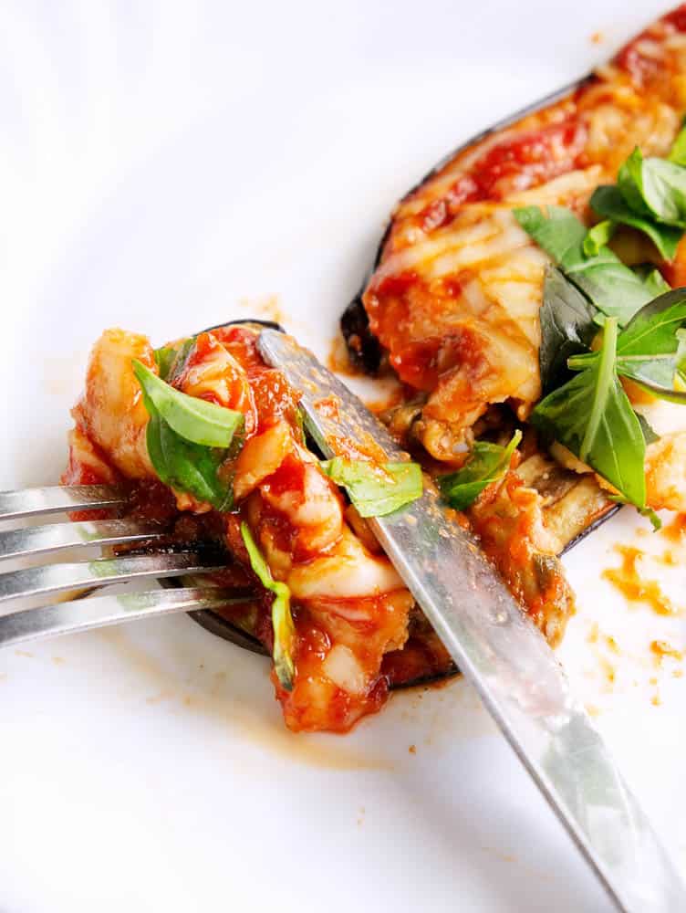 closeup bite of healthy eggplant parmesan with knife and fork