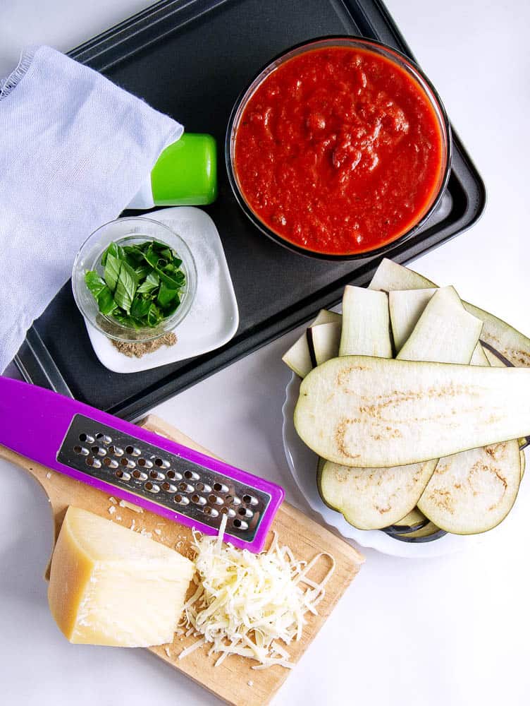ingredients for healthy eggplant parmesan: marinara sauce, basil, cheese, eggplant slices