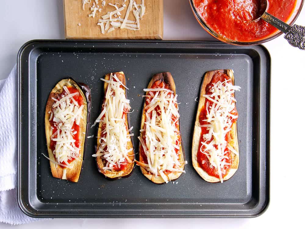 healthy eggplant parmesan - eggplant slices on baking sheet topped with marinara sauce and cheese, before roasting