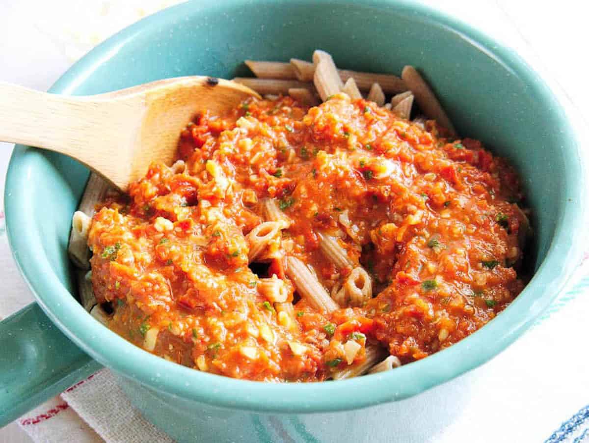 Pasta sauce tossed with pasta in a blue bowl.