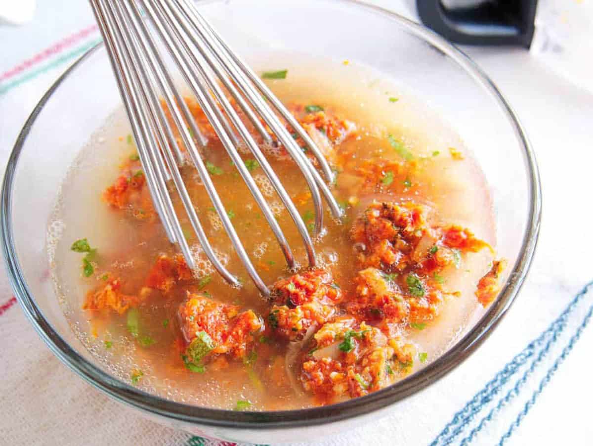 Sun dried tomatoes, basil, spices mixed with water in a glass bowl.
