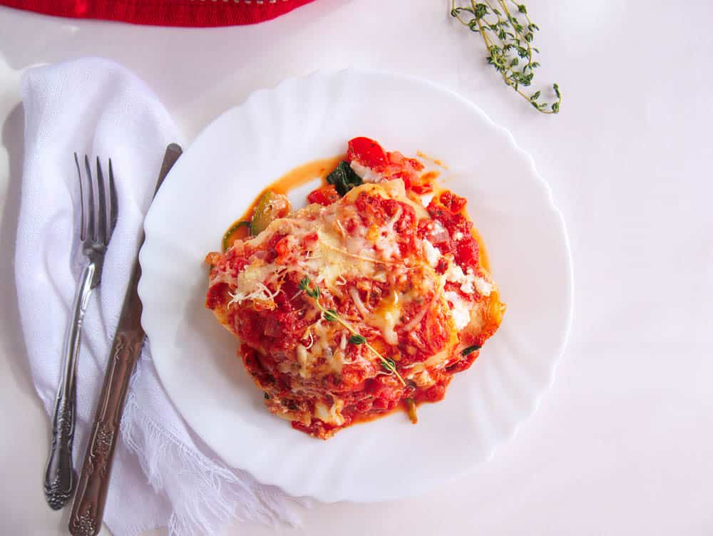 Top shot of a healthy vegetable lasagna served on a white plate with a knife and fork
